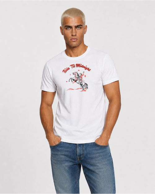 Male model wearing the white "Ride 'Til Midnight" western cowboy graphic t-shirt with jeans, cropped torso shot, hands in pockets